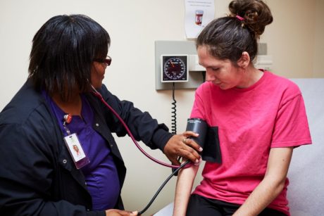 A Black woman medical professional measures a young white patient's blood pressure