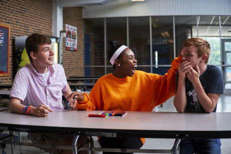A group of middle school-age students of different racial backgrounds have an animated conversation in a cafeteria