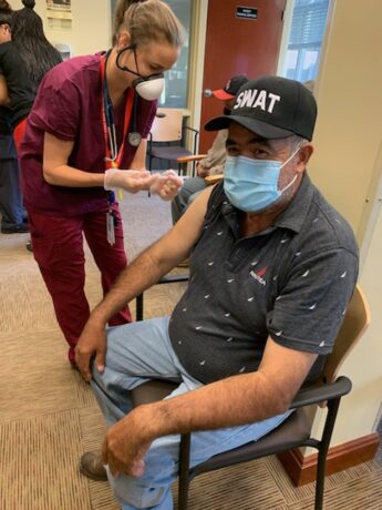 A person with a mask and hat receives a vaccine.