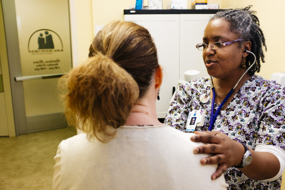 A health care provider listens to a patient with a stethoscope.