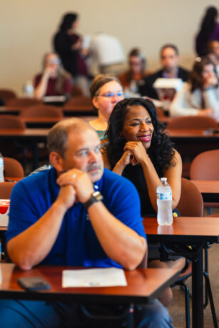 two people with their hands folded while sitting look onward to someone talking